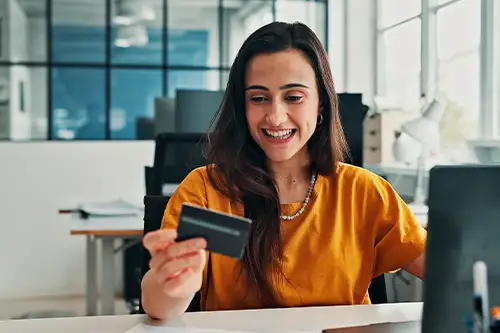A woman sitting at a computer in an office, holding a credit card
